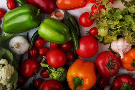 top view of fresh ripe vegetables as tomatoes colorful bell peppers green chili pepper garlic green onions and broccoli on white backgroundの写真素材