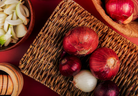 top view of red and white onions in basket plate with sliced white one in bowl and black pepper seeds on red backgroundの写真素材