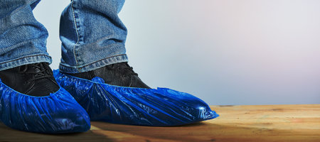 Horizontal shot of men's legs in blue shoe covers worn over classic shoes on gray background,...