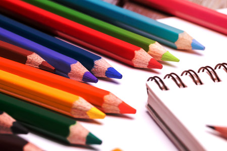 many colorful crayons and pencils scattered on a white paper sheetsの写真素材