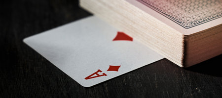 Horizontal shot of ace of diamonds is under a deck of cards on a wooden table.の写真素材