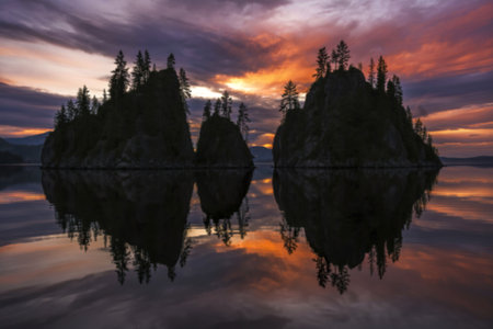 A photograph of several dark, silhouetted islands reflected in the mirror-like surface of a tranquil lakeの写真素材
