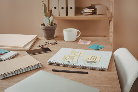 A wooden desk with various office supplies, including notebooks, a plant, a mug, and sticky notes.