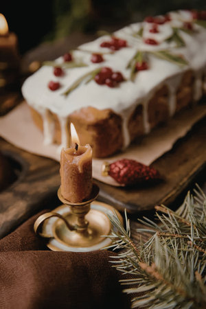 a cake with white icing and red berries on a wooden board with a candle in the foreground