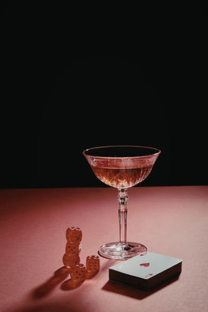 a glass of red wine, dice, a gummy bear and a playing card on a pink surface