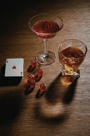 A still life of two glasses of drink, a deck of cards, and dice on a wooden table.