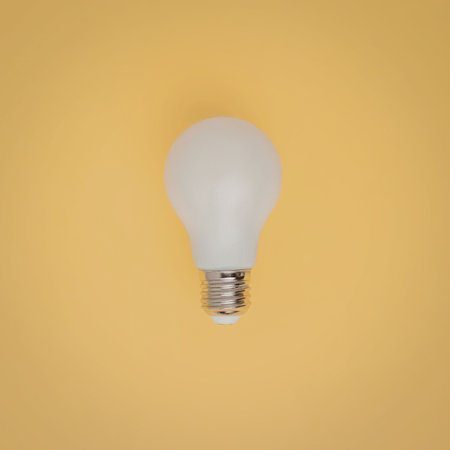 A white light bulb against a bright yellow background, symbolizing ideas and innovation.の写真素材