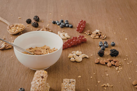 A bowl of oatmeal with a spoon, surrounded by fresh fruits and nuts on a wooden table.の写真素材