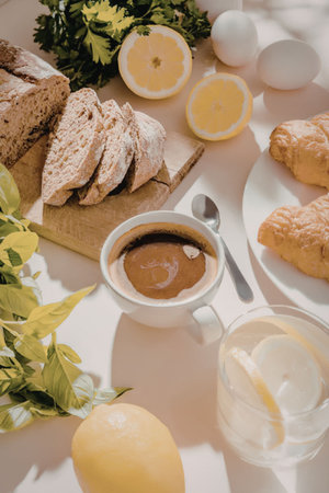 A breakfast spread featuring sliced bread, croissants, coffee, and fresh lemons on a white table.の写真素材