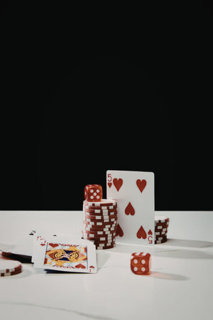 A collection of poker chips, playing cards, and dice on a white table against a black background.