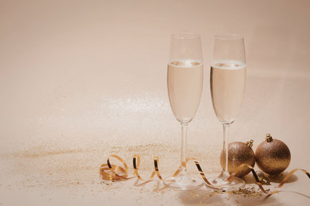 Two champagne glasses filled with bubbly champagne, surrounded by festive decorations and ornaments on a shiny surface.の写真素材
