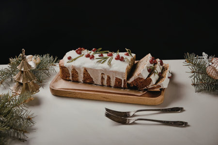 A festive Christmas fruitcake with white icing, decorated with red berries and green leaves, served...