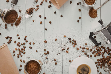 An overhead shot of coffee beans scattered on a white wooden table with cups and coffee-making...