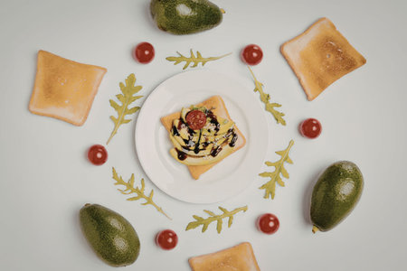 A plate of bruschetta surrounded by fresh tomatoes, avocados, and herbs on a white background.の写真素材