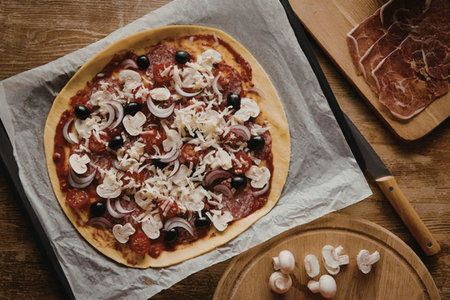 A homemade pizza with various toppings, including mushrooms, olives, and cheese, placed on a wooden...