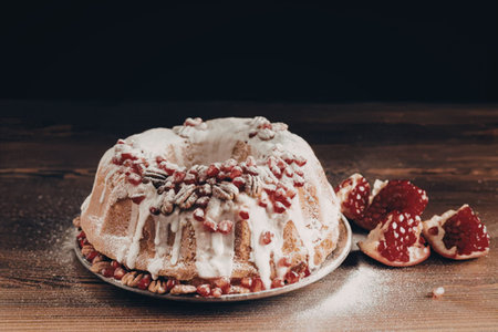 A beautifully decorated bundt cake with white icing and pomegranate seeds, accompanied by fresh...