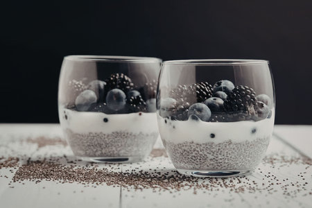 Two glasses of chia seed pudding topped with blueberries and blackberries on a white table.の写真素材