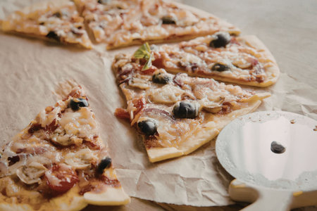 A tasty pizza cut into slices on parchment paper with olives and cheese