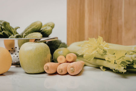 A selection of fresh fruits and vegetables arranged on a kitchen counter, including apples, carrots, celery, and leafy greens.の写真素材