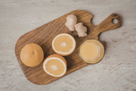 A wooden cutting board with oranges, ginger and juice on a marble countertopの写真素材