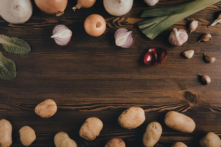 A variety of fresh potatoes and vegetables arranged on a wooden table, including onions, garlic, and pomegranate seeds.の写真素材