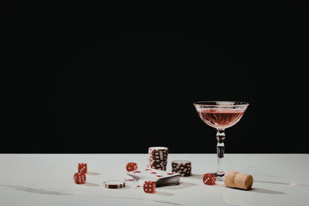 A martini glass filled with red liquid, surrounded by dice and a wine cork on a table.