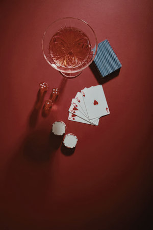 A glass of red liquid, a deck of cards, dice, and poker chips on a red surface