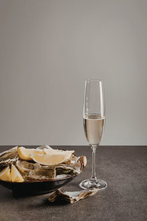 A glass of champagne next to a plate of oysters with lemon wedges
