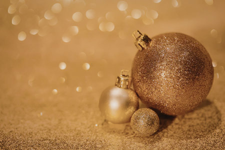 A close-up of three golden Christmas ornaments on a glittering gold background with bokeh lightsの写真素材