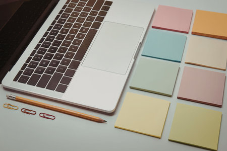 A laptop keyboard and colorful sticky notes on a desk with a pencil and paper clips