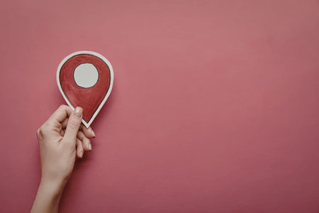 A hand holding a red location pin on a pink background
