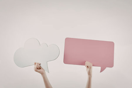 Two hands holding a white cloud-shaped speech bubble and a pink rectangular speech bubble against a...