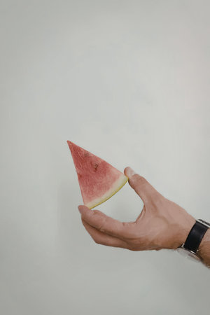 A hand holding a slice of watermelon against a plain backgroundの写真素材
