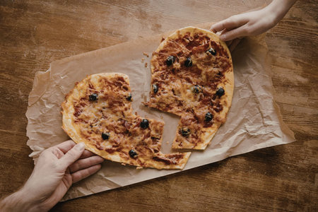 A heart shaped pizza on brown paper being held by two hands on a wooden table