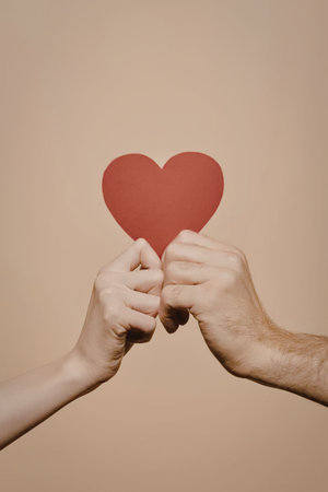 Two hands holding a red heart cutout against a beige background