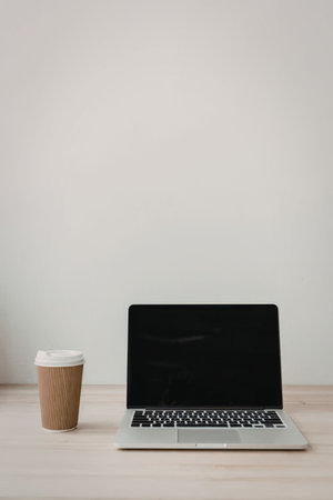 A laptop and a coffee cup on a wooden desk against a white background