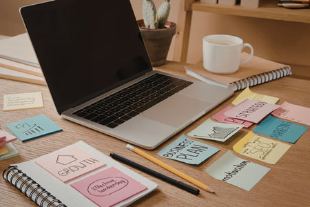 A laptop, notebooks, pencils, and sticky notes on a wooden desk