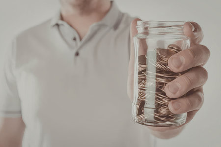A man in a white polo shirt holding a jar filled with coins.