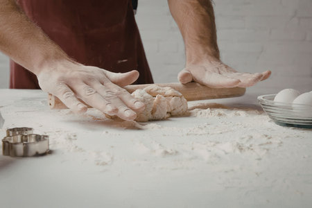 a man wearing a red apron is kneading dough on a floured surface with a bowl of eggs and cookie...
