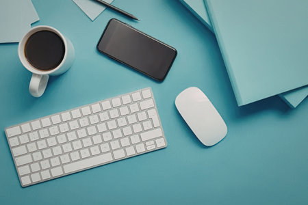 A neatly arranged office workspace with a white keyboard, mouse, black smartphone, and a cup of...