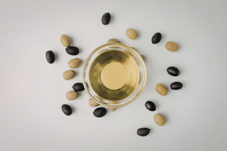 A small glass bowl of olive oil surrounded by green and black olives on a plain white surfaceの写真素材