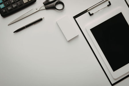 A workspace with a clipboard, calculator, scissors, pen, and notepad on a white desk.