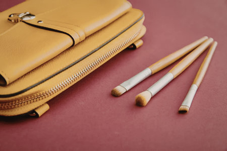 A yellow leather pouch with makeup brushes on a pink background