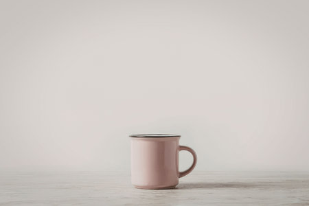 A pink mug with a handle on the right side sits on a light-colored table against a white background.の写真素材