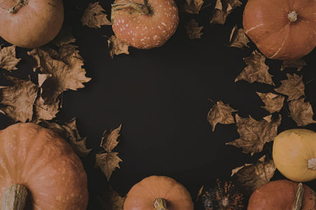 An arrangement of pumpkins and dried leaves on a dark surface, likely for fall or autumn decoration.