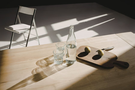A serene still life arrangement featuring a glass of water, a bottle of water, and a cutting board...