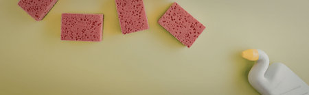 A group of pink sponges and a white and yellow cleaning supply on a green surface
