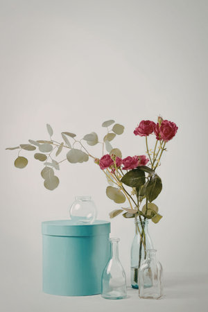 A serene still life arrangement featuring pink roses in glass vases alongside a teal container and...