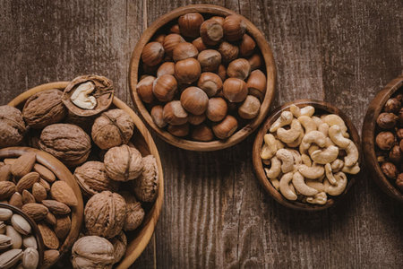 An assortment of nuts arranged in wooden bowls on a rustic wooden table, showcasing a mix of...