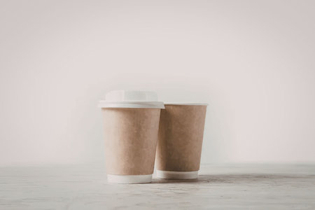 Two brown disposable coffee cups with white lids on a gray surface